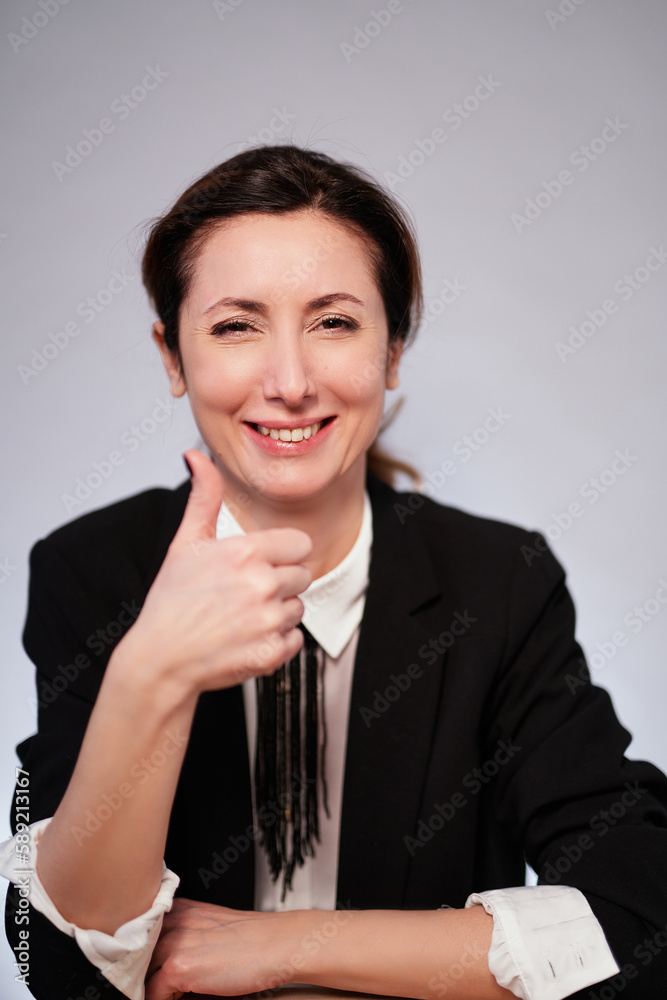 Making thumbs up gesture. Adorable business lady in black jacket posing on isolated background. Happy cheerful manager woman in dark suit smiling and looking at camera. High quality photo Making thumbs up gesture. Adorable business lady in black jacket posing on isolated background. Happy cheerful manager woman in dark suit smiling and looking at camera. High quality photo
