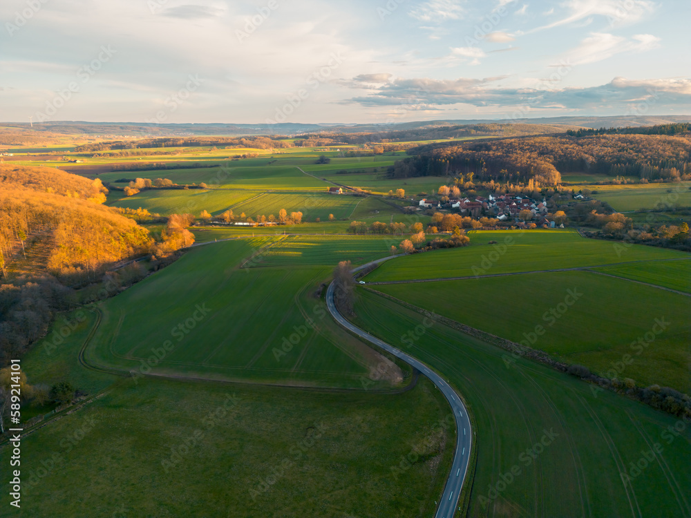 Aerial view of road going towards the little village in the countryside at sunset