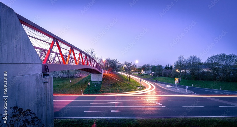 Naklejka premium Long exposure of the lights of the cars on the road with a pedestrian bridge at sunset