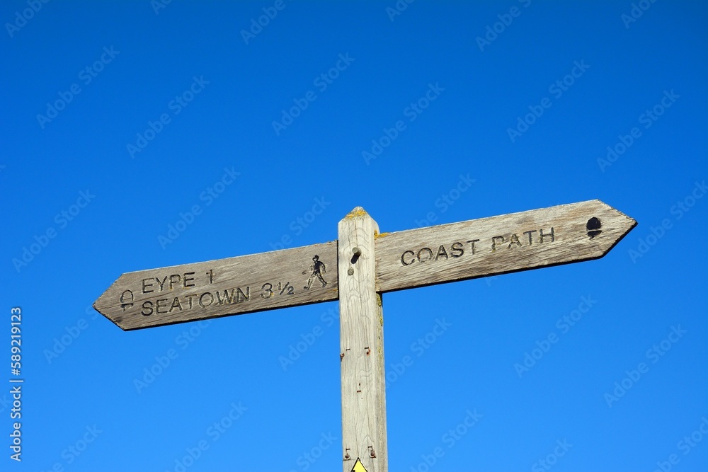 Wooden coast path sign with walking route to Eype and Seaton against a blue sky, West Bay, Dorset, UK, Europe
