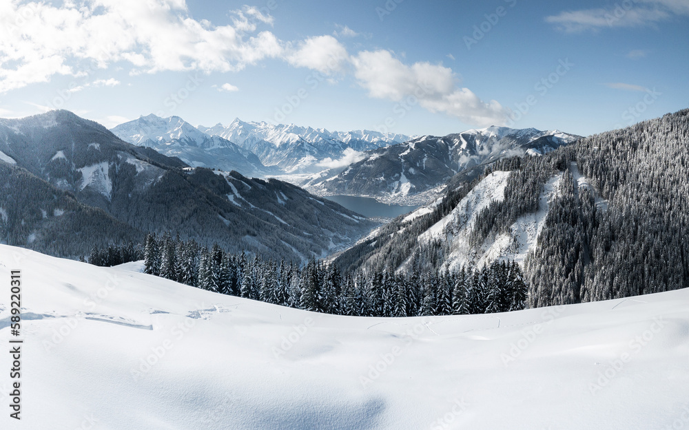 Panoramic view of winter wonderland mountain scenery with the alpine town of Zell am See and Zeller See Lake on cold winter day with clouds and blue sky, Zell am See, Pinzgau, Salzburg Land, Austria