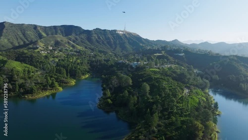 Scenic aerial above blue Hollywood lake reservoir with deep blue water on green Hollywood hills, Los Angeles California USA. Scenic aerial shot expensive houses in green forest on sunny summer day 4K
