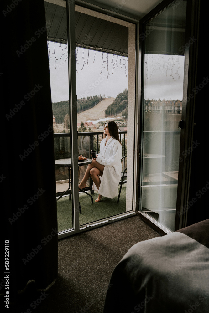 A woman in a white bathrobe eats a croissant and drinks coffee in a hotel in the mountains.Resort vacation concept