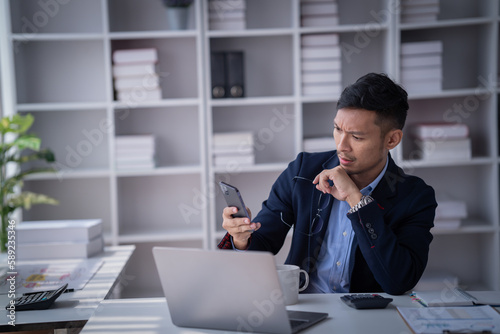 Portrait of Smiling young male employee feel euphoric sitting at his desk using smart phone at office.