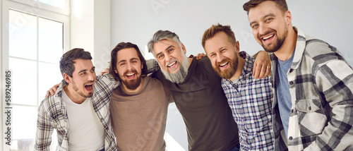 Group of happy male friends standing and hugging. Portrait of cheerful hipster men posing together and smiling at camera indoors. Male friendship, best friends concept