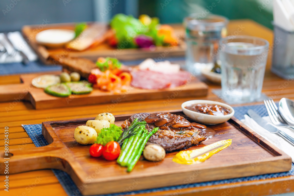 Tasty meal of grilled steak, smoked salmon, and vegetables at rustic outdoor restaurant. Perfect for a summer lunch or dinner with a tropical feel.