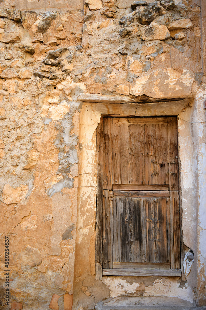 An old wooden door in a wall of vernacular construction with stone and mortar worn by the passage of time, typical of some villages of Spain