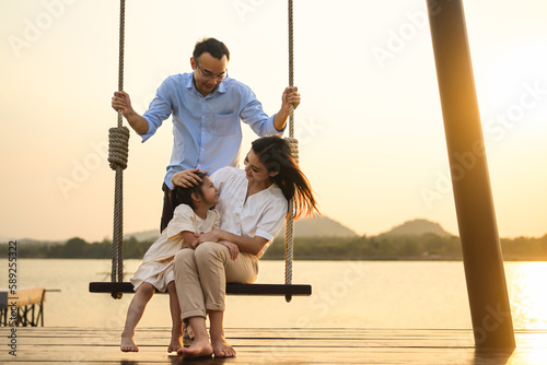 Family enjoying with outdoor activities sitting on swing with sunset #589255322