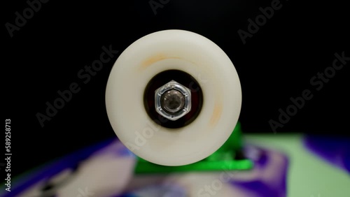 Rapidly spinning skateboard wheel steadily loses speed and comes to a stop. Close macro shot shows wheel nut and bearings, skate truck is visible in soft focus. photo