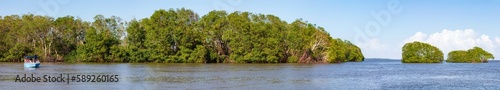 Belize Rivers, mit einem Speedboot auf dem Fluss durch die Mangroven-Landschaft, blauer Himmel mit Wolken, ein Panorama.