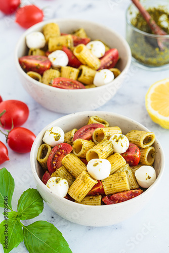 Rigatoni pasta with pesto  tomatoes and mozzarella in white bowl. Italian cuisine concept.