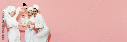 Photography Three emotional, happy, beautiful young girls in bathrobes drinking champagne, having fun against pink background