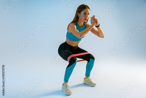 Athletic woman trains legs with fitness elastic band on studio background. High quality photo