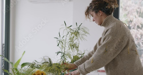 female doing new bouquet. Girl working in flower shop studio. Female florist artist cleans flowers for a beautiful bouquet, workplace view. High quality 4k footage
