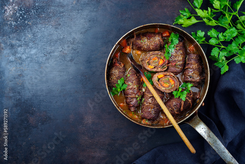 Traditionelle langsam gegarte deutsche Wagyu Rinderrouladen mit Gemüse und Speck serviert in würziger Bratensoße als Draufsicht in einer Kupfer Kasserolle