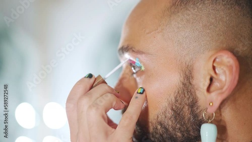 Young black transgender man applying make-up mascara eyeshadows, LGBTQ Man in fashion clothing wearing makeup, womanlike transsexual man with make up on face, looking fashion glamorous