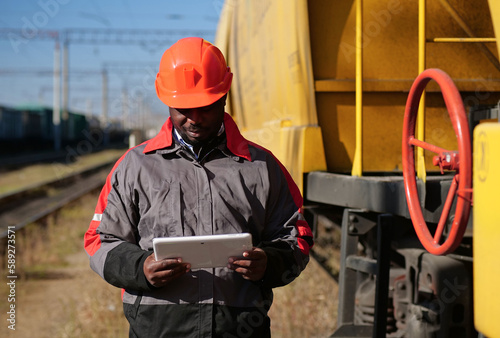 Inspector of wagons at freight train station looks in tablet computer photo