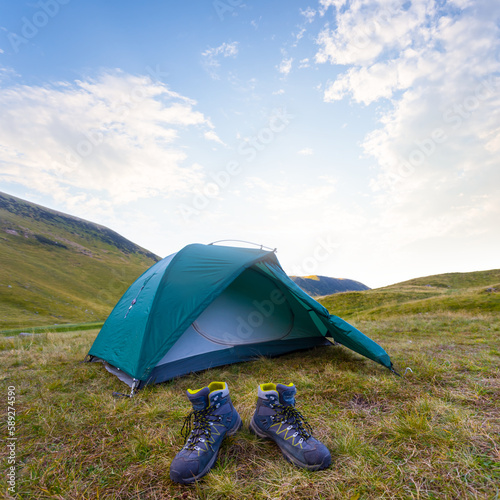 pair of boots near touristic tent in mountain valley, summer outdoor travel scene
