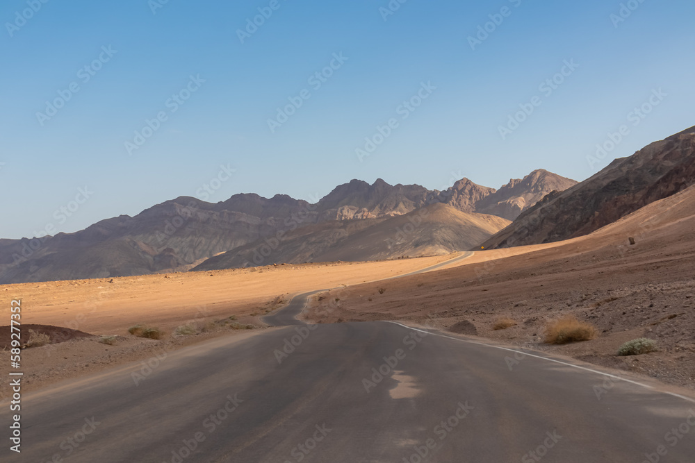 Panoramic view of endless empty road leading to colorful geology of multi hued Artist Palette rock formations in Death Valley National Park near Furnace Creek, California, USA. Black mountains
