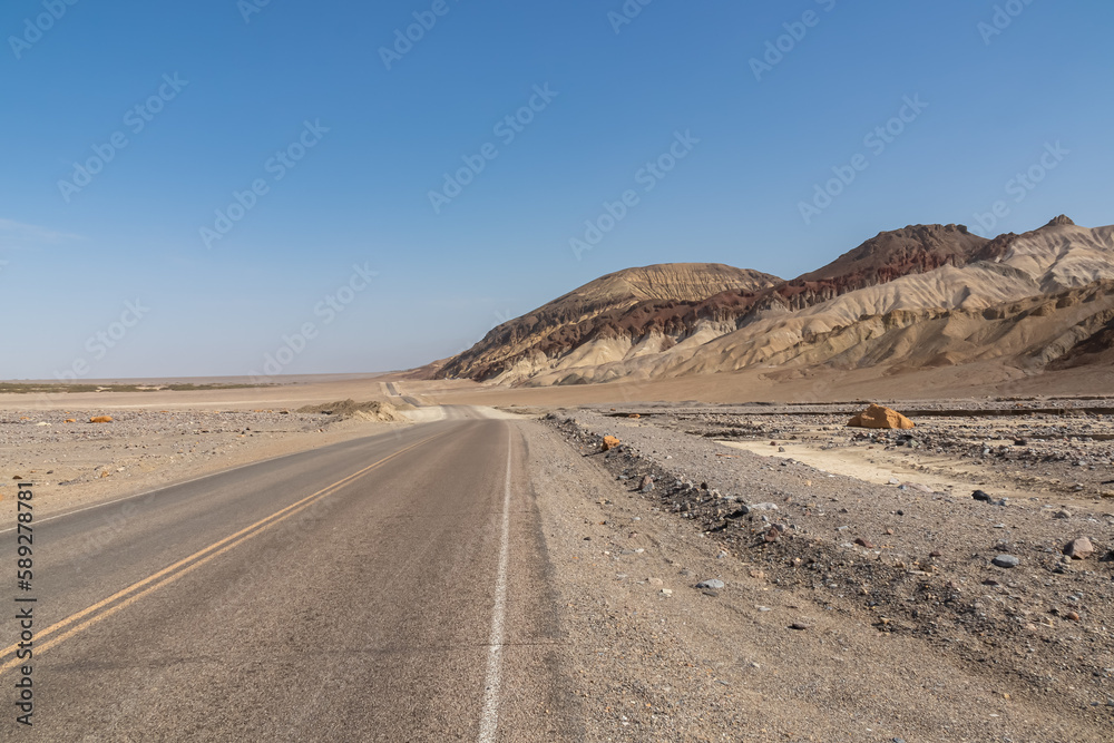 Panoramic view of endless empty road leading to colorful geology of multi hued Artist Palette rock formations in Death Valley National Park near Furnace Creek, California, USA. Black mountains