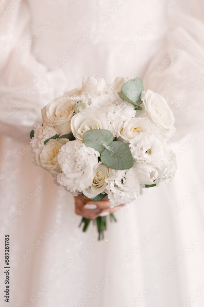 Beautiful wedding white bouquet of roses in the hands of the bride