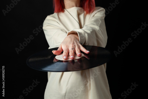 Charming happy young redhead girl in a white oversized sweatshirt holds a vinyl record. Isolated on black.