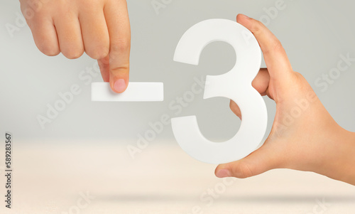 Minus three. The number three and the minus symbol in a hand close-up on a light gray background. The concept of removal or taking away