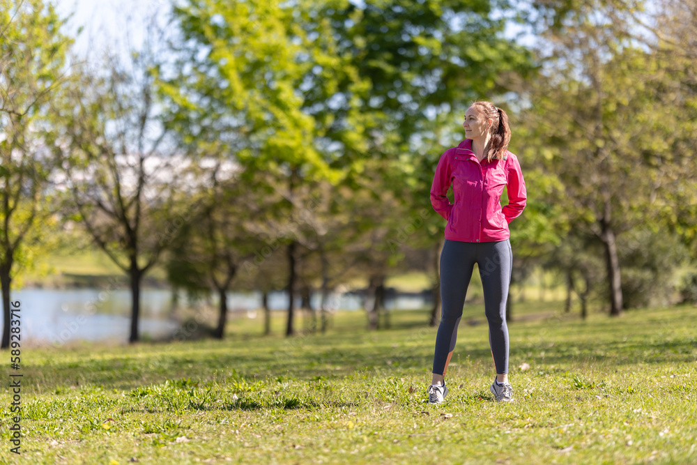 An adult smiling woman in sports clothes standing on the field and looking to the side An adult smiling woman in sports clothes standing on the field and looking to the side