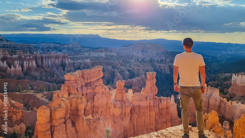 Man in front of Thors Hammer during sunrise on Navajo Rim hiking trail Bryce Canyon National Park, Utah, USA. Scenic golden hour view of sandstone hoodoos rock formation in amphitheatre on sunny day