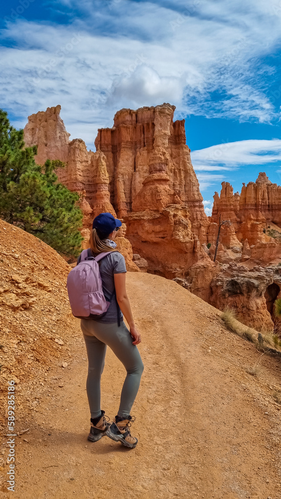 Naklejka premium Backpacker woman hiking on Peekaboo trail with scenic view of hoodoo sandstone rock formations in Bryce Canyon National Park, Utah, USA. Pine trees surrounded by natural amphitheatre in sunny summer