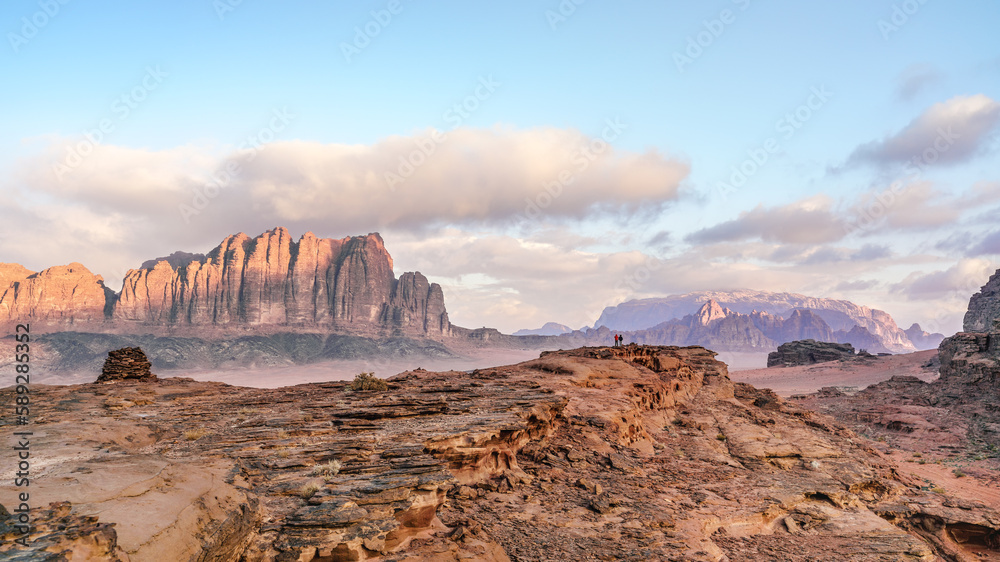 Red sandstone rocks formations in Wadi Rum - two small persons at distance (also known as Valley of the Moon) desert, Jordan. Morning sun shines to mountains background