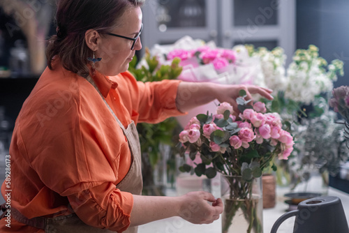 At the flower shop, the professional female florist expertly creates a gorgeous bouquet of pink roses and peonies, perfect for any occasion.