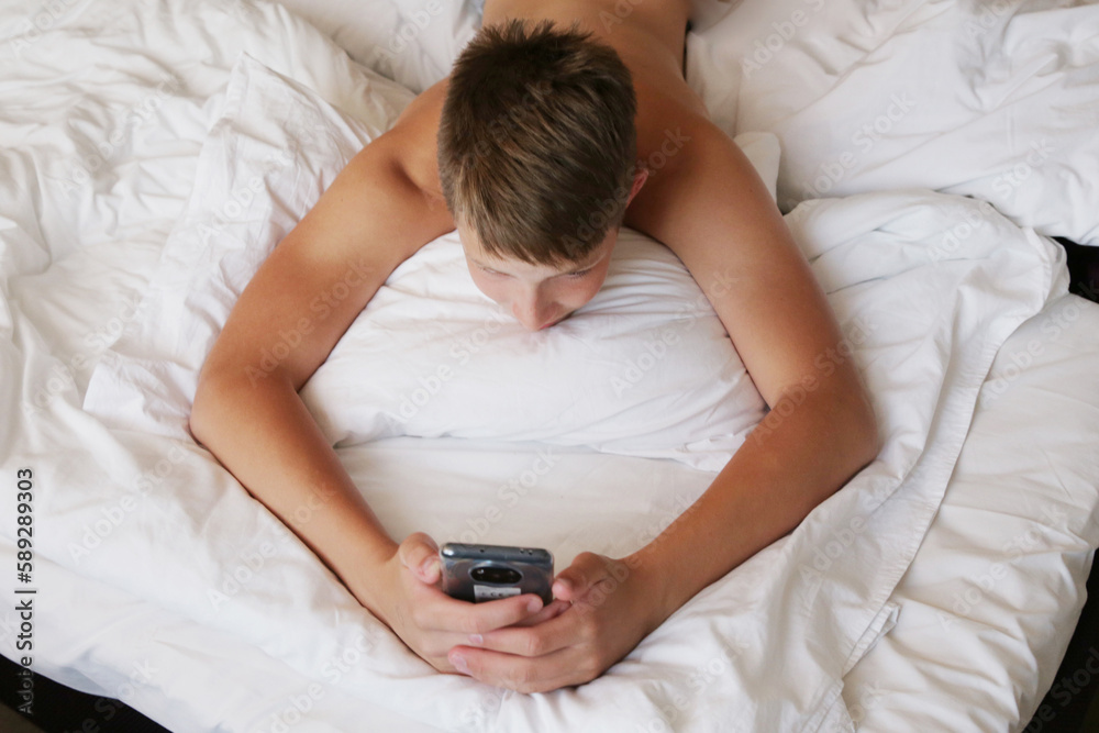 The boy lies on the bed with the phone. The boy lies on the bed with the phone.