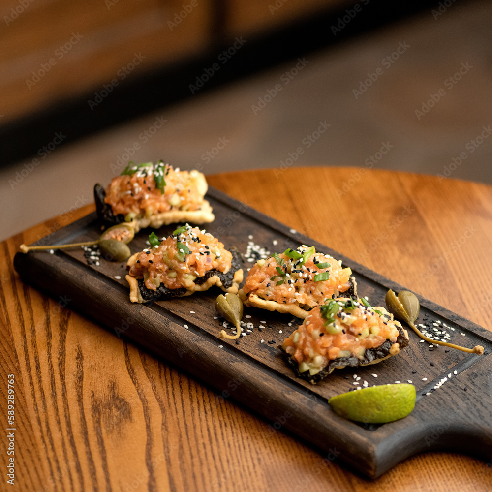 Snacks with red fish paste are decorated with green onions and sesame seeds on wooden plank on table. Cold appetizers. Sandwiches with salmon. Side view. Wooden background. Copy space.