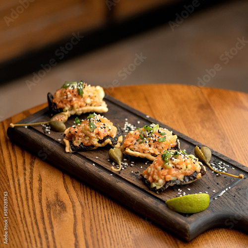 Snacks with red fish paste are decorated with green onions and sesame seeds on wooden plank on table. Cold appetizers. Sandwiches with salmon. Side view. Wooden background. Copy space.