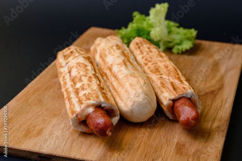 three french hot dogs on a wooden board on a black background, fast food.