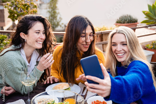 Happy women friends taking selfie at vegan food restaurant outdoors - Focus on center girl face