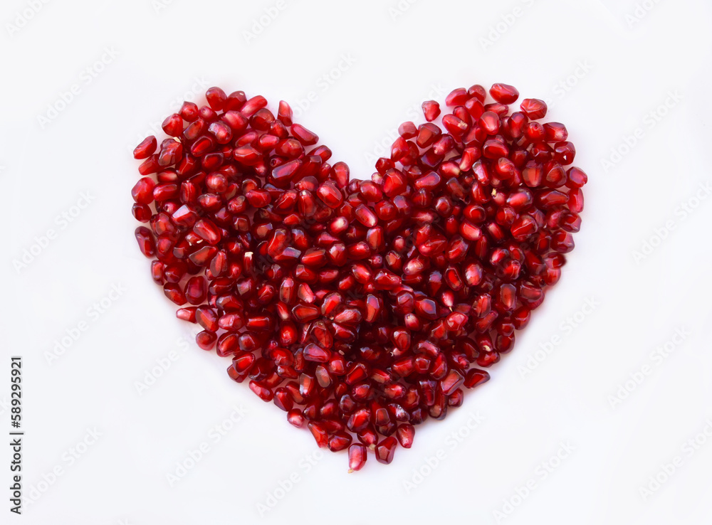 Pomegranate seeds shaped as a heart on white background, bright kernels of granatum are showing beautiful shades of red. Semitransparent juicy arils of ripe tasty fruit, fresh healthy food concept. Pomegranate seeds shaped as a heart on white background, bright kernels of granatum are showing beautiful shades of red. Semitransparent juicy arils of ripe tasty fruit, fresh healthy food concept.