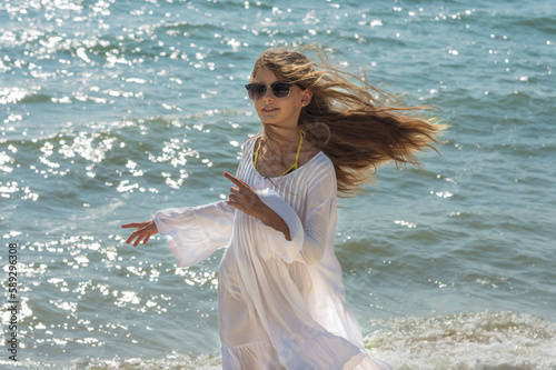 Pretty young lady in white dress is dancing on the beach.