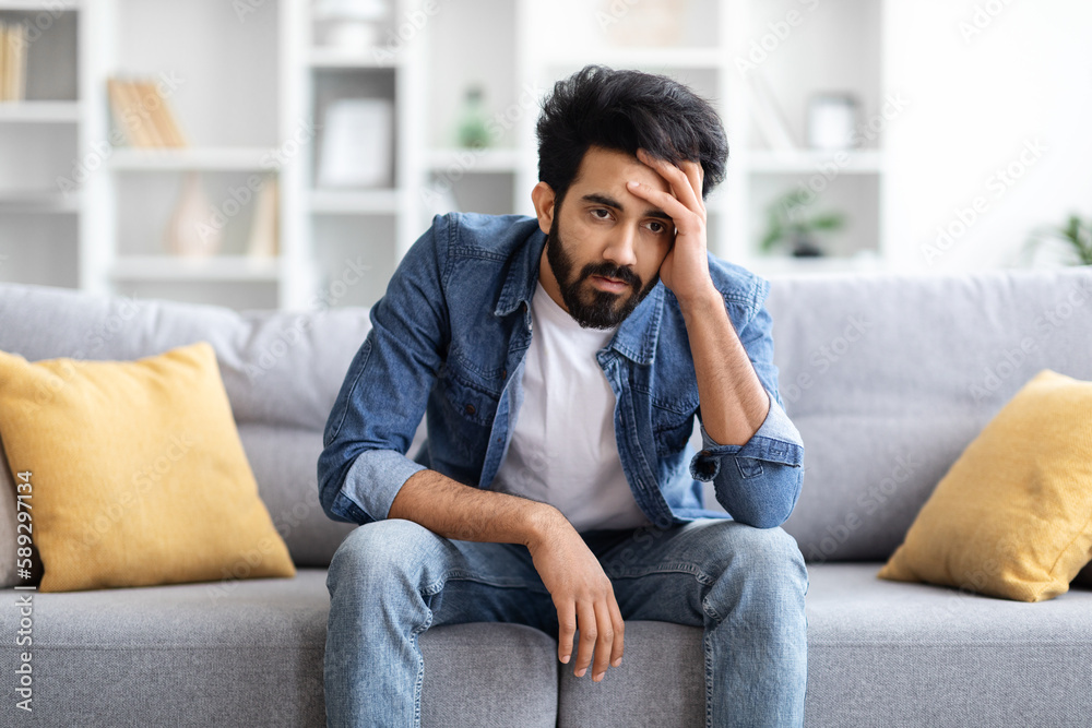 Portrait Of Depressed Young Indian Man Sitting On Couch At Home Portrait Of Depressed Young Indian Man Sitting On Couch At Home