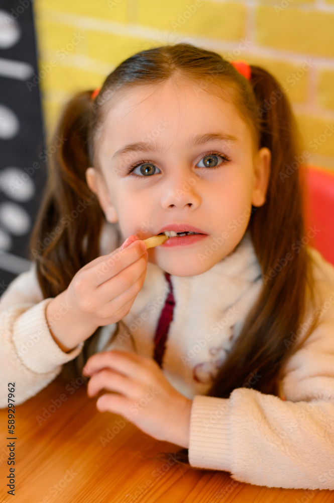 A small and beautiful girl is eating french fries in a cafe. A small and beautiful girl is eating french fries in a cafe.