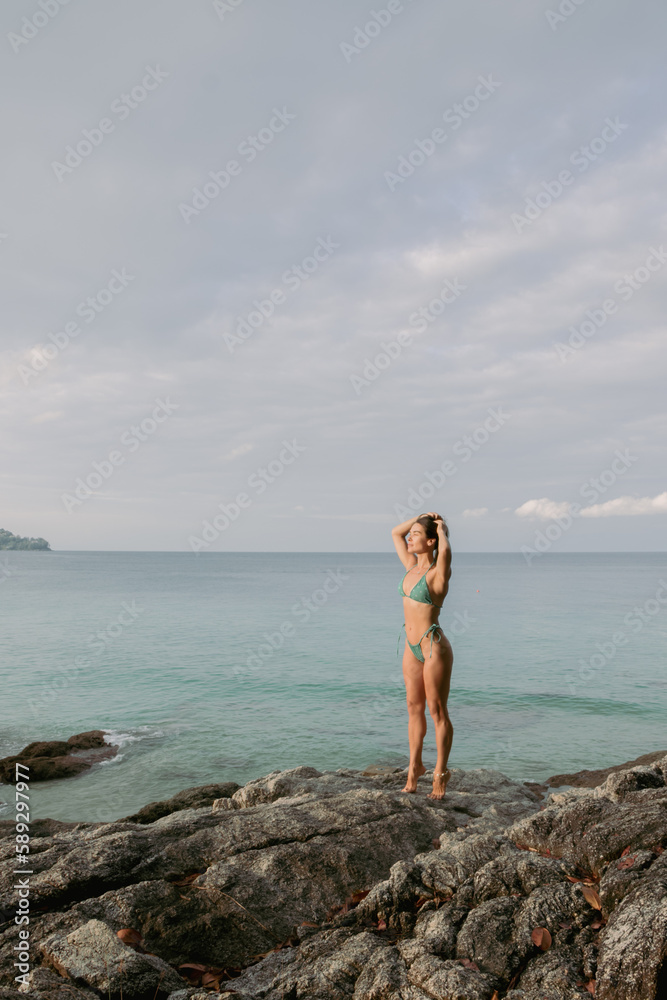 a young girl in a swimsuit is standing by a cliff on the seashore