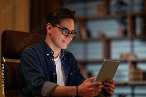Happy young guy businessman using digital tablet at dark office