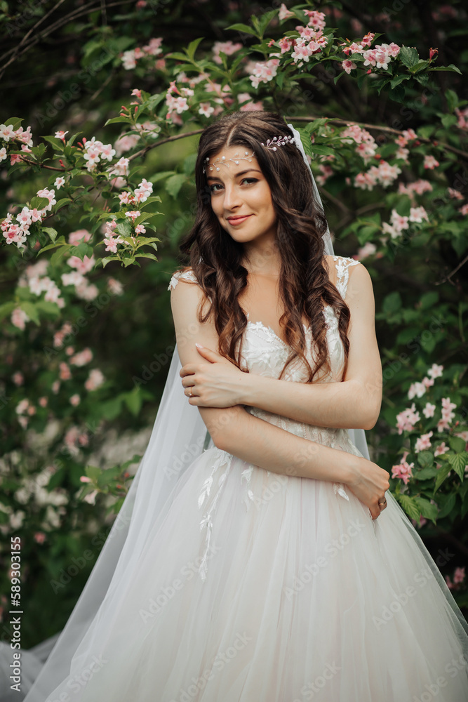 A beautiful bride with long curly hair in a chic dress, smiling, holding her wedding bouquet, looking into the lens. Portrait of the bride. Spring wedding. Natural makeup A beautiful bride with long curly hair in a chic dress, smiling, holding her wedding bouquet, looking into the lens. Portrait of the bride. Spring wedding. Natural makeup