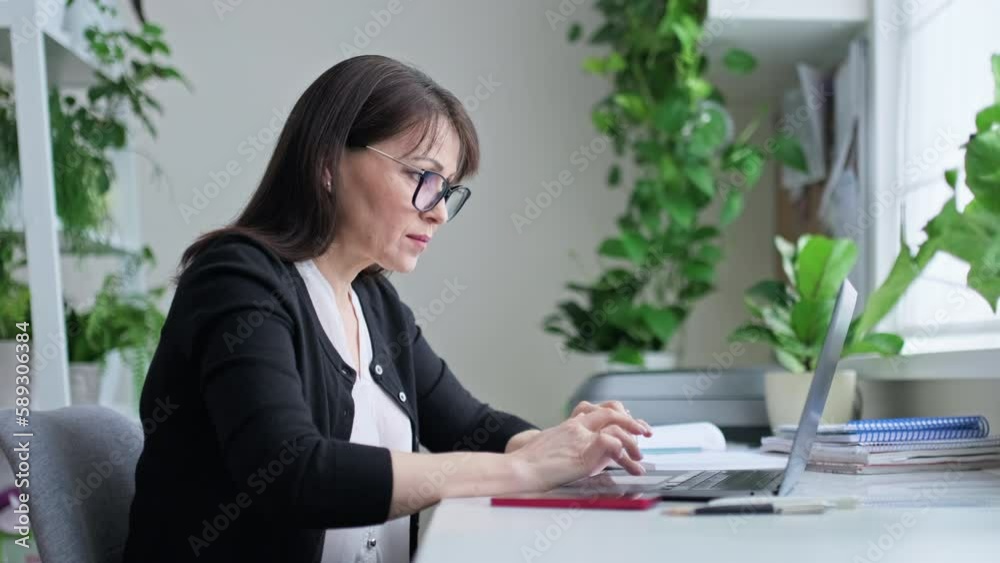 Middle aged woman working in home office using smartphone laptop Middle aged woman working in home office using smartphone laptop