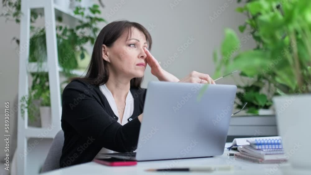 Tired middle aged woman sitting at workplace, taking off her glasses looking out window Tired middle aged woman sitting at workplace, taking off her glasses looking out window