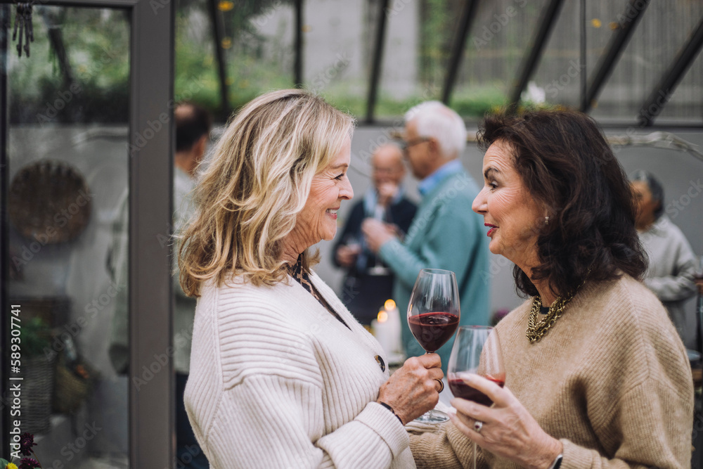 Smiling senior woman with wineglasses talking to female friends at dinner party Smiling senior woman with wineglasses talking to female friends at dinner party