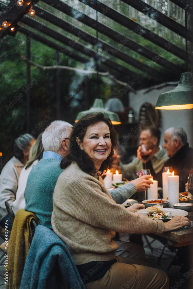 Portrait of happy retired woman sitting on chair during dinner party with friends Portrait of happy retired woman sitting on chair during dinner party with friends