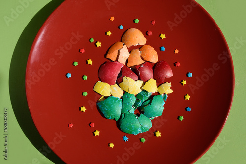 Pieces of colourful crushed easter eggshell folded in the shape of an egg Isolated on a red plate on a green background