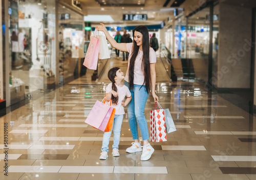 young mother and daughter holding shopping bags, shopping in the mall. Family shopping.